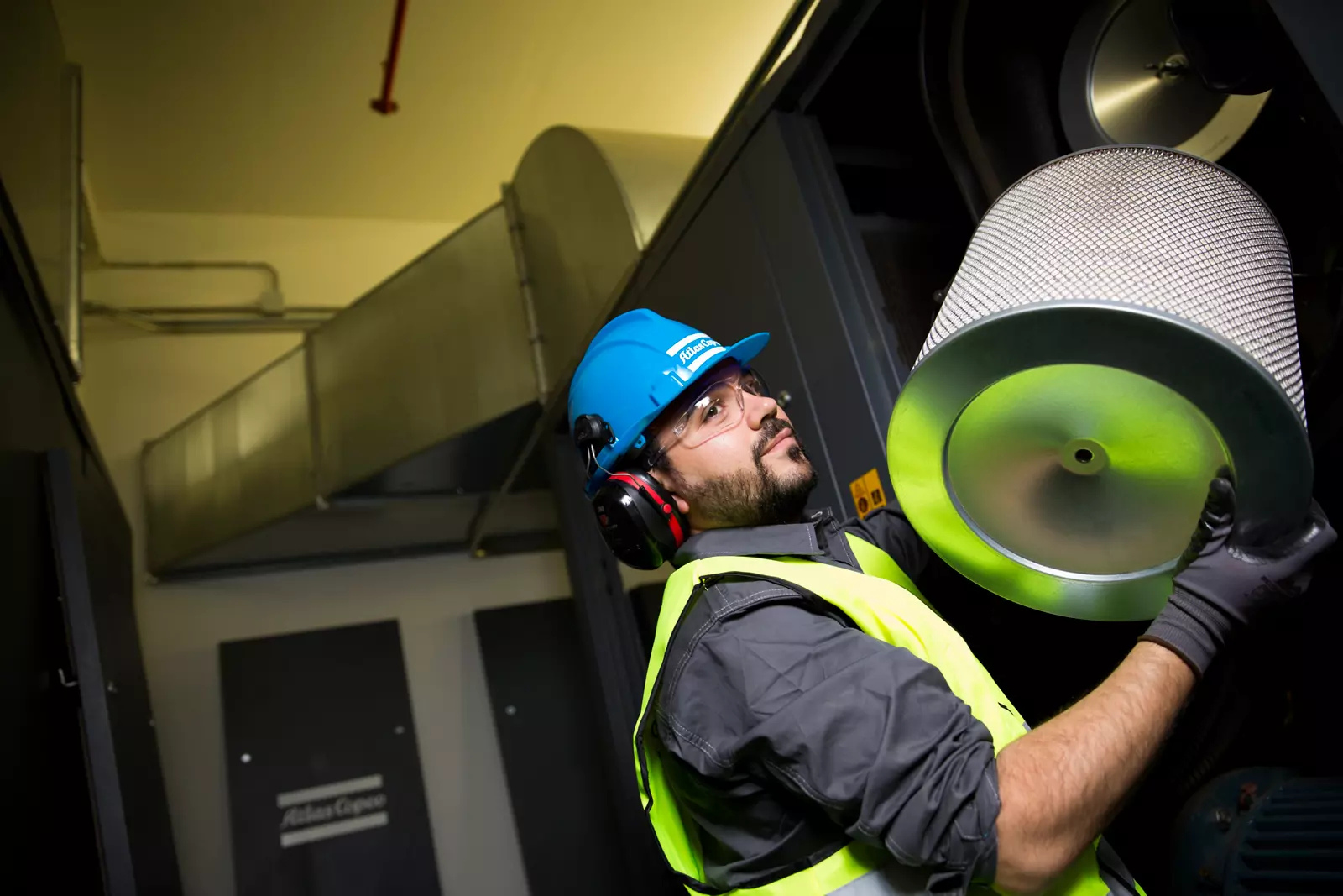 Atlas Copco service engineer removing a compressor intake filter element during a planned maintenance visit